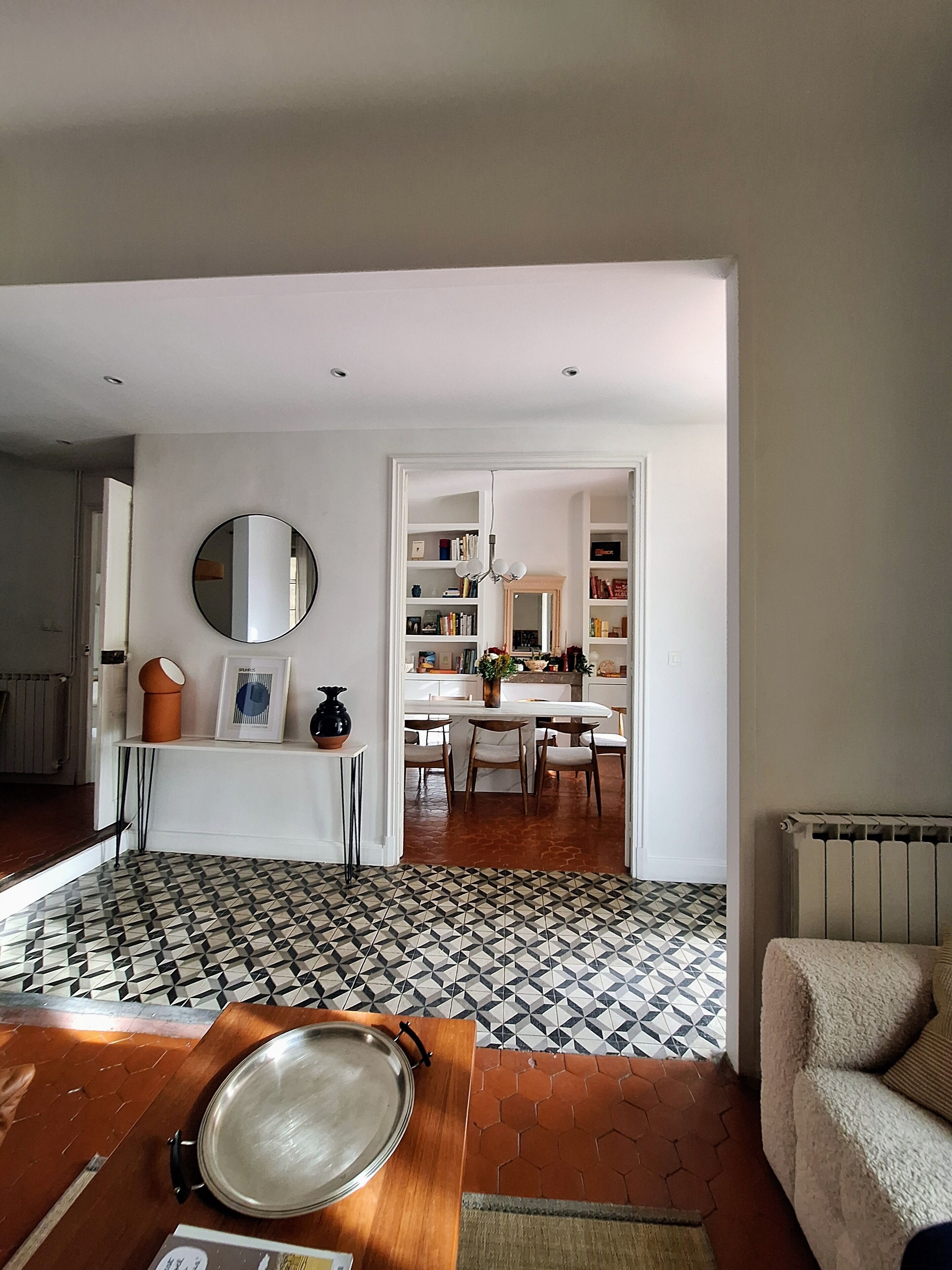 A modern living room with a patterned floor, a dining area with a table and chairs, and a kitchen visible through an open doorway.