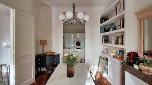 Un vaste espace dédié à la salle à manger, avec une table en marbre, des chaises en bois, un lustre et une bibliothèque remplie de livres et d’objets décoratifs.