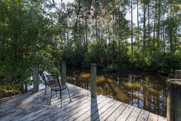 Une jetée en bois avec une chaise, entourée d’une forêt dense et d’une rivière paisible.