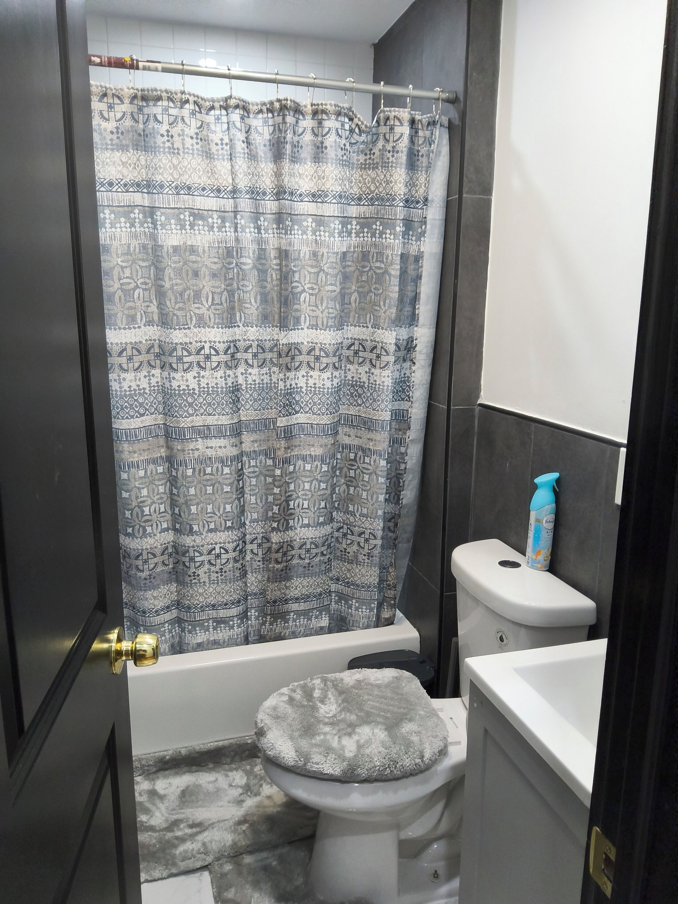 A bathroom with a patterned shower curtain, a toilet with a grey seat, and a white bottle of hand soap on the wall.