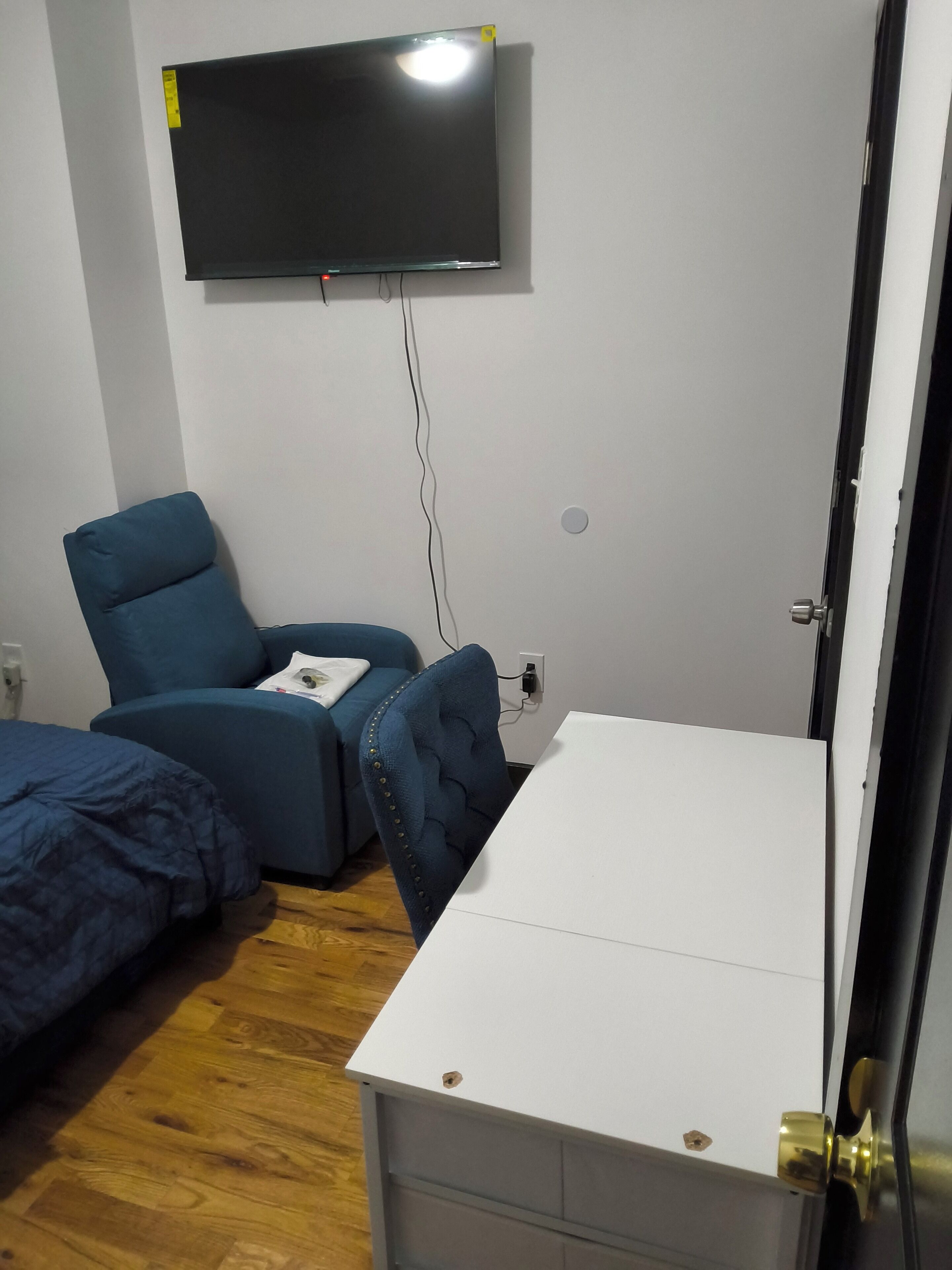 Ein Schlafzimmer mit Bett, Schreibtisch, Stuhl, Wandfernseher und einer Tür.