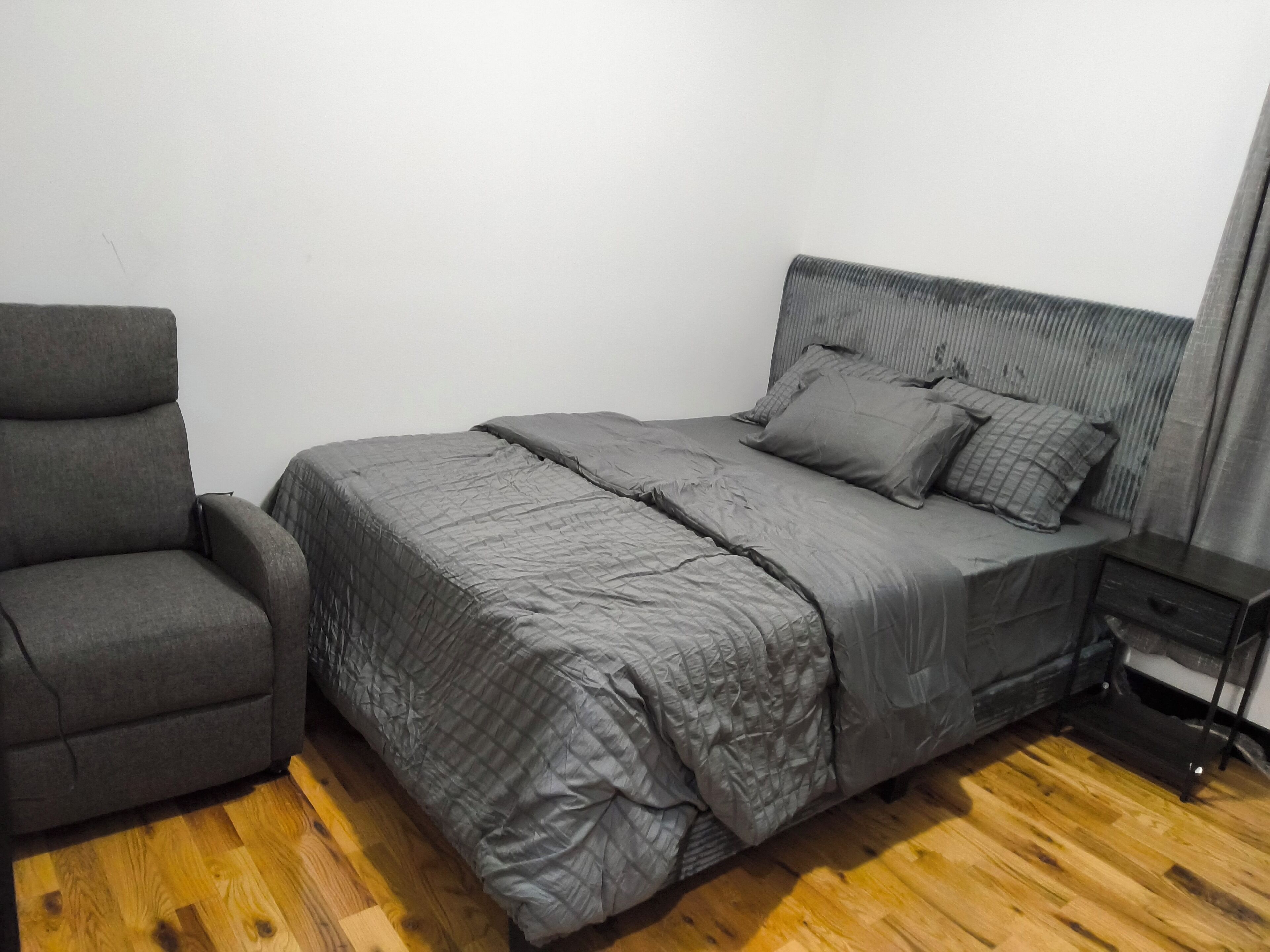 A bedroom with a bed, a chair, and a nightstand.