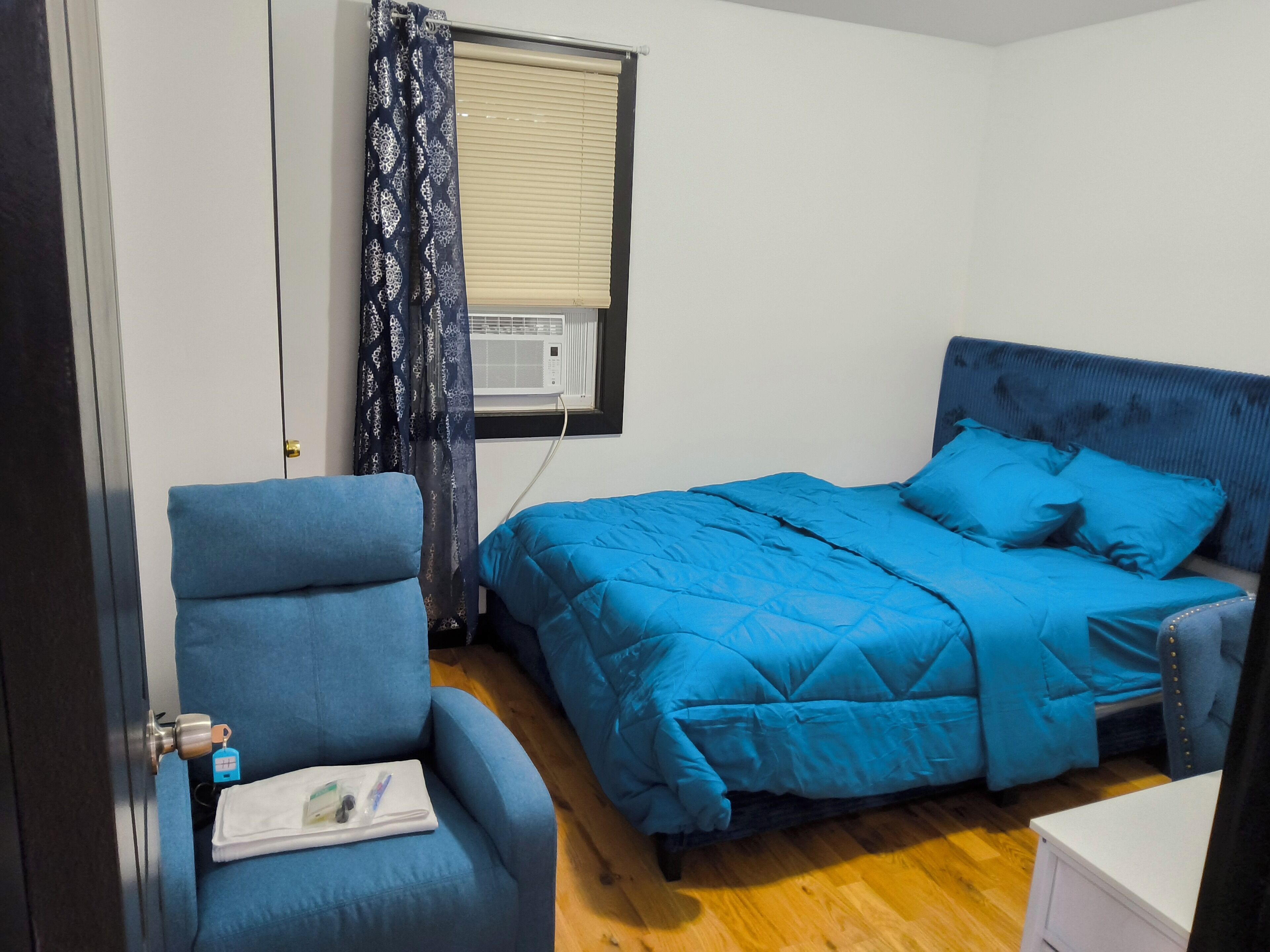 Un dormitorio con una cama, una silla y una ventana con cortina.