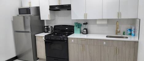 A modern kitchen with white cabinets, a stainless steel refrigerator, a black stove, and a sink with a gold faucet.