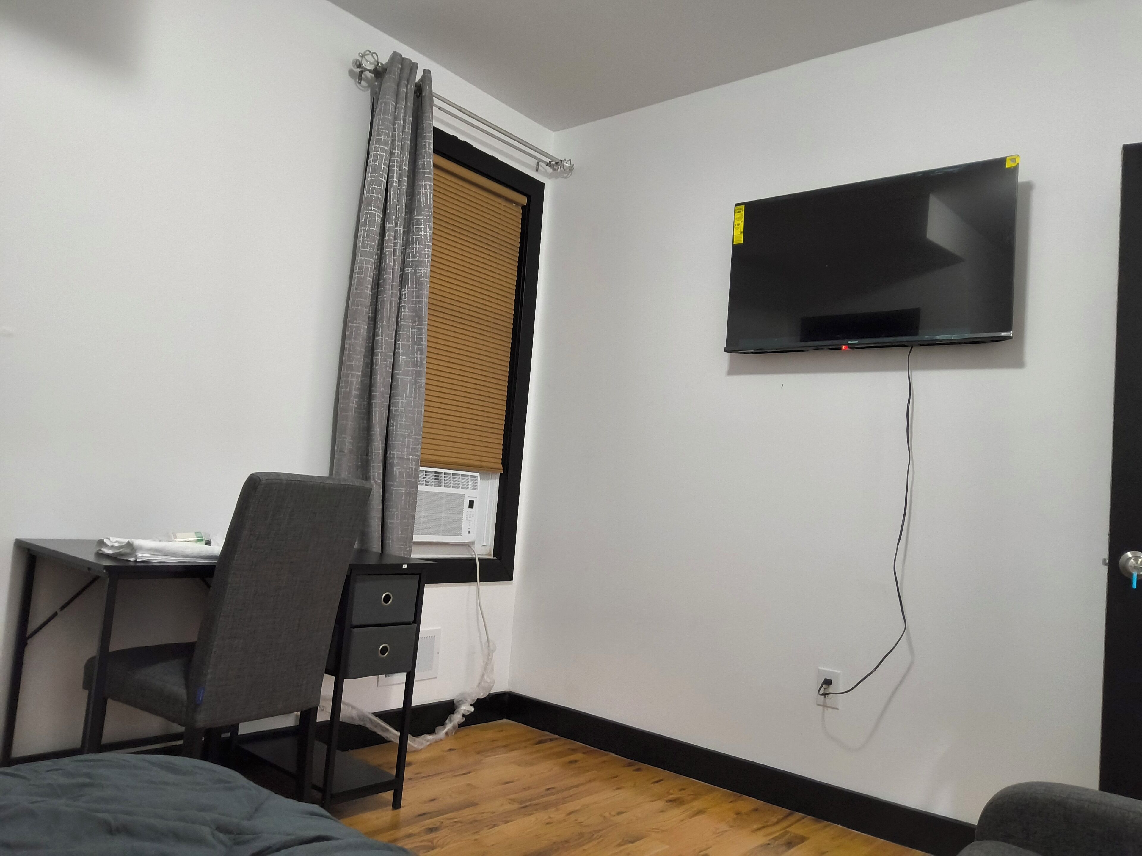 Una habitación pequeña y ordenada, con escritorio, silla y televisor montado.