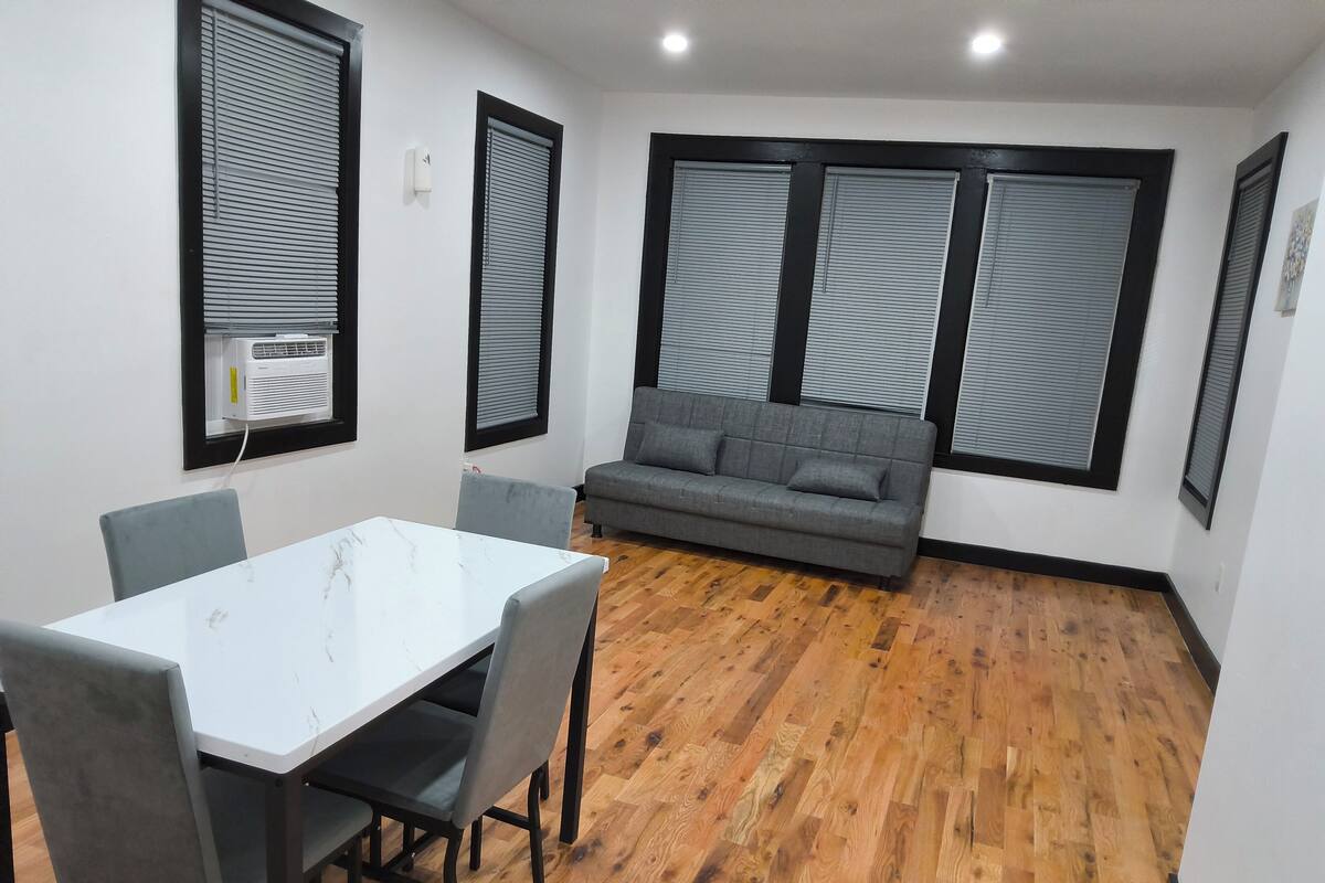 A room with a white table and chairs, a grey sofa, and a wooden floor.