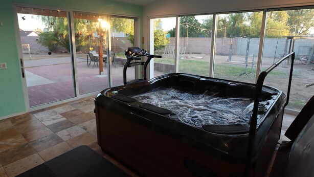 A hot tub in a room with large windows, a ceiling fan, and a patio area with a table and chairs. - Relaxing Corner -Huge backyard - Hot Tub and Views (Tucson)