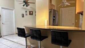A kitchen with a central island, two bar stools, a refrigerator, and a ceiling fan. - Relaxing Corner -Huge backyard - Hot Tub and Views (Tucson)