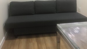 Ein dunkel gefärbtes Sofa vor einer weißen Wand, ein Tisch mit Glasplatte und ein Holzboden.