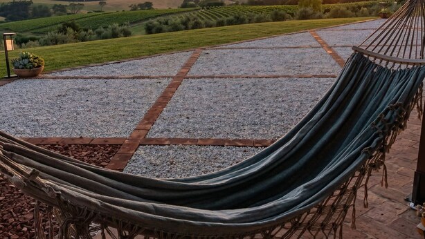 A hammock on a paved patio with a view of a sunset over rolling hills. - Private Hilltop Villa with Sea Views in the Heart of Maremma, Tuscany (Scansano)
