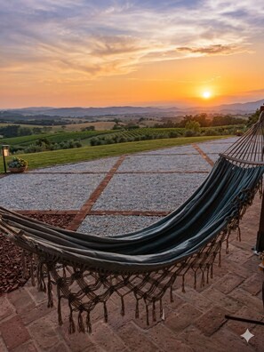 A hammock on a paved patio with a view of a sunset over rolling hills. - Private villa on a hill with ocean views in the heart of the Maremma, Tuscany   (Scansano)