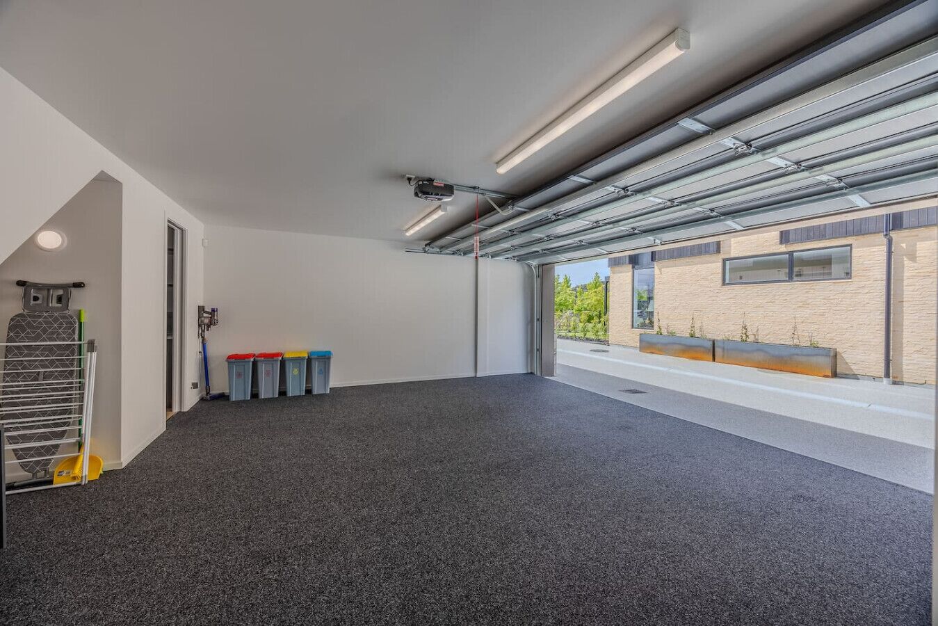 A spacious room with a grey carpet, a large window with a view of the outside, and a door leading to another area.