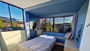 A bedroom with a bed, a window seat, and a view of the outside. - Cozy Apartment (Santa Tecla)