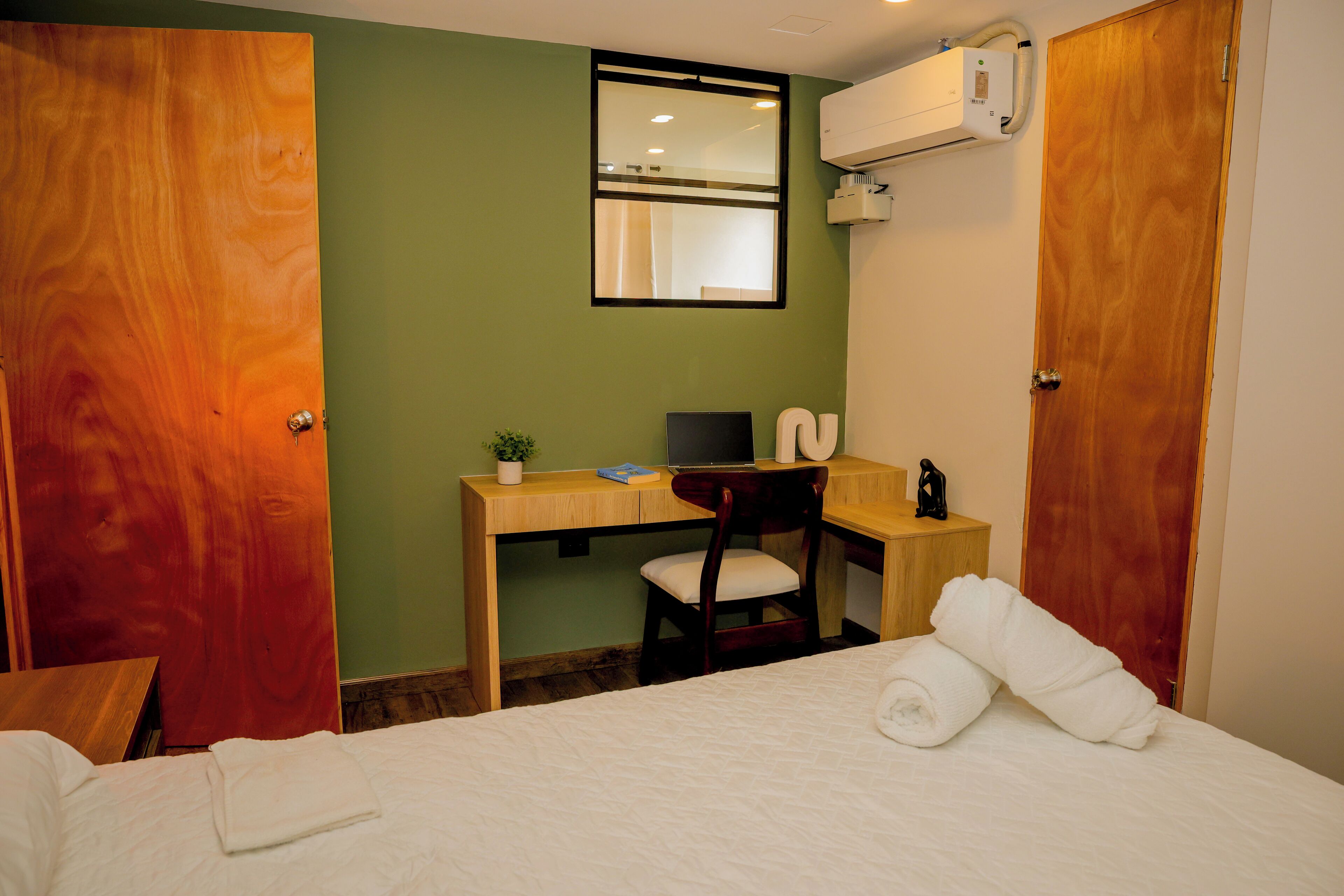 A hotel room with a bed, a desk with a computer, a chair, and a window.