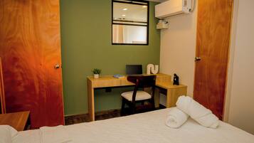 A hotel room with a bed, a desk with a computer, a chair, and a window.