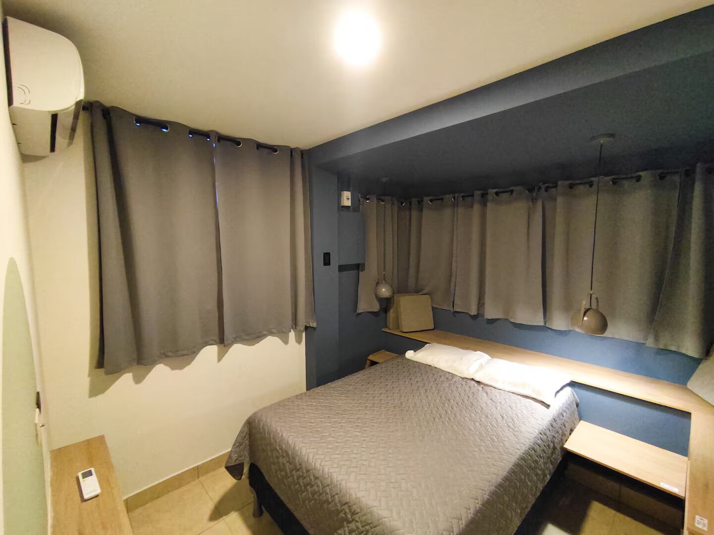 Un dormitorio con cama, mesitas de noche, cortinas, lámpara y estante en la pared.