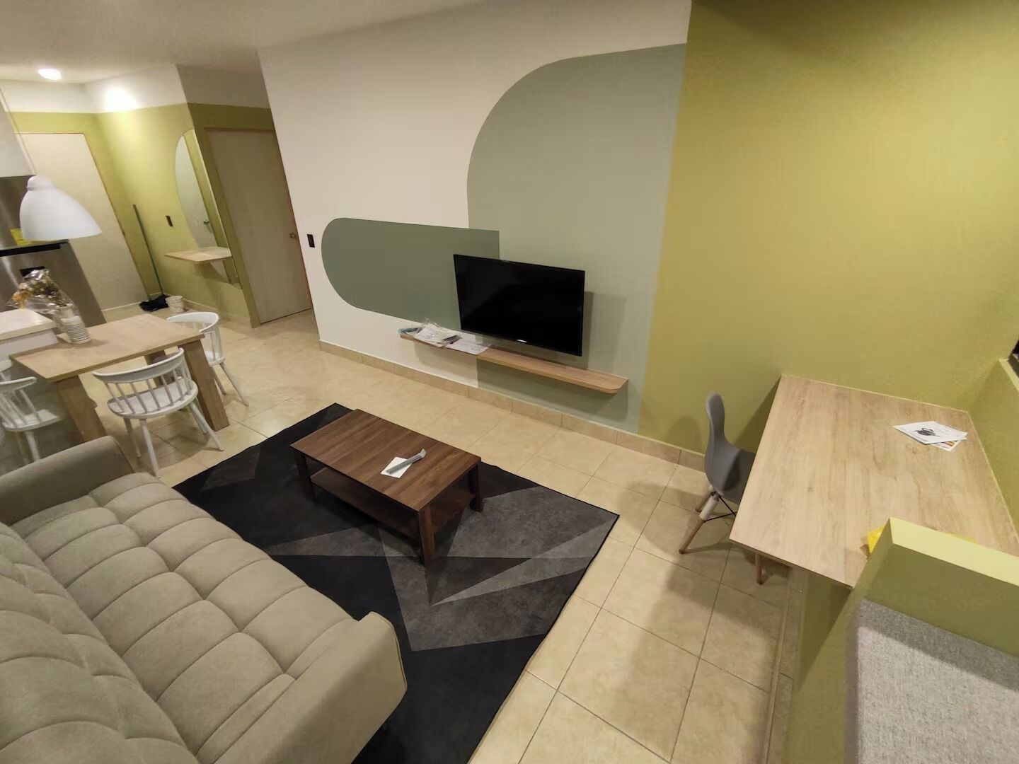 A modern living room with a sofa, coffee table, TV, and a small dining area.