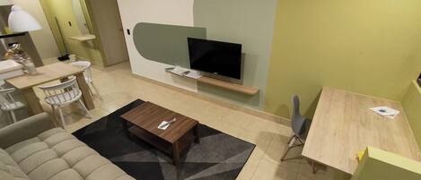 A modern living room with a sofa, coffee table, TV, and a small dining area.