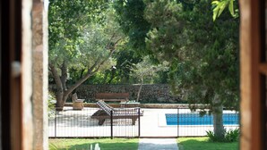 A view through a window of a courtyard with a stone wall, a bench, and a pathway. - Sa Carrotja - Traditional villa with pool near the sea (Manacor)