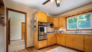 A kitchen with wooden cabinets, a built-in oven, and a window with a view of trees.