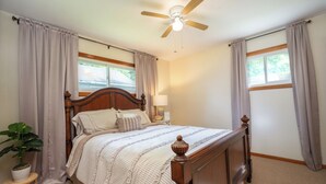 A bedroom with a wooden bed, a ceiling fan, and a window with curtains.