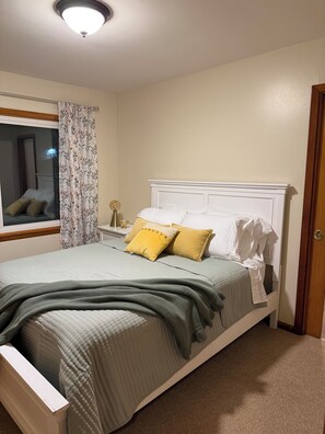 Una cama bien tendida con un cabecero blanco, ropa de cama verde y dos almohadas, una amarilla y otra blanca.