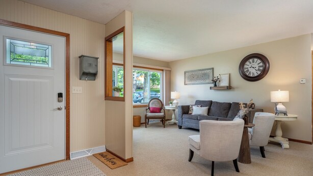A living room with a sofa, chairs, a coffee table, a clock, and a door with a window.