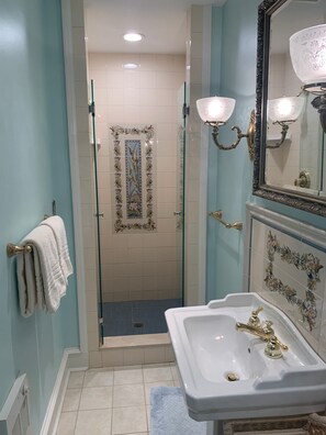 A bathroom with a glass-enclosed shower, a white sink with a gold faucet, and a mirror with ornate gold detailing. - The Chancellor's House B&B (Bedford)