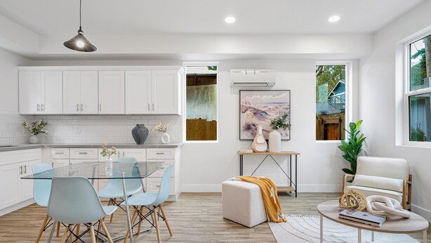 Una cocina moderna con armarios blancos, una mesa de comedor de vidrio y una zona de estar acogedora con sofá y reposapiés.