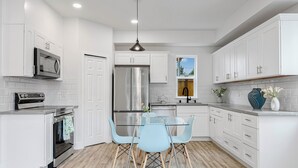 A modern kitchen with white cabinetry, stainless steel appliances, a glass dining table, and light blue chairs. - Brand New 2-bedroom 2-bathroom house with WiFi, AC in delightful Seattle (Seattle)