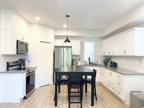 Une cuisine moderne avec des meubles blancs, des appareils en acier inoxydable, un îlot central doté de chaises et un luminaire suspendu.