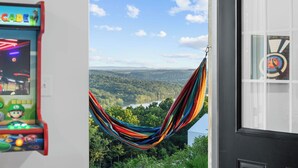 A Nintendo 64 arcade machine, a hammock overlooking a forested landscape, and a door with a circular window. - Lux Lakeview • Pool, Hot Tub, Game Room, EpicViews (Omaha)
