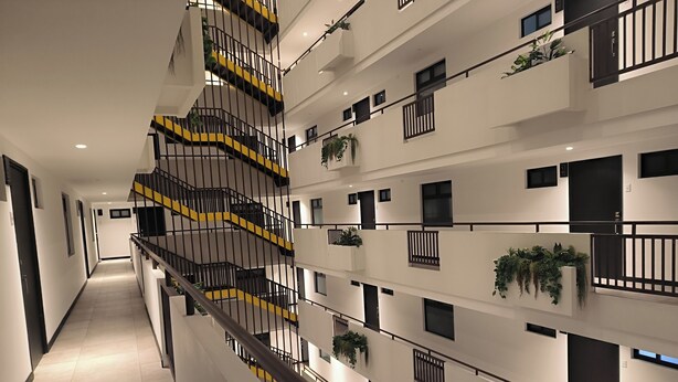 A multi-level residential building with a central staircase, balconies with plants, and a clean, modern design.