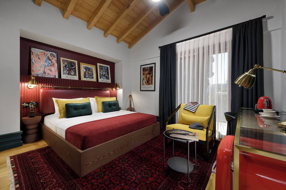 A bedroom with a wooden bed, a red and black patterned rug, a yellow armchair, and a red cabinet.