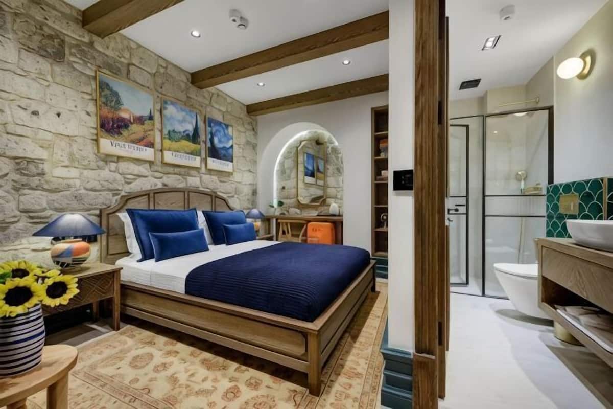 A bedroom with a stone wall, a wooden bed, a nightstand, a lamp, and a vase with sunflowers.