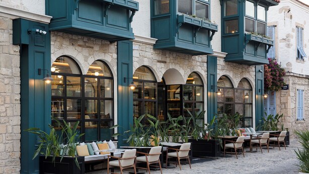 A building with a stone facade, large arched windows, and outdoor seating with tables and chairs. - Tinspiro Alaçatı (Cesme)