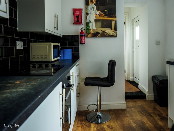 A kitchen with a microwave, a fire blanket, and a stool.