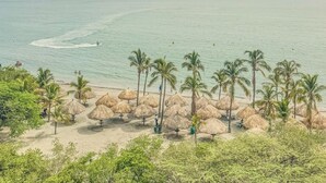 A beach with palm trees and thatched umbrellas, a clear sky, and calm sea. - New KeyPöint: Long stays in Pözos Colorados! (Santa Marta)