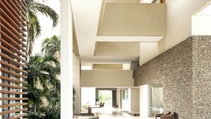 A spacious lobby with a high ceiling, stone wall, and a seating area with chairs and a bench. - New KeyPöint: Long stays in Pözos Colorados! (Santa Marta)