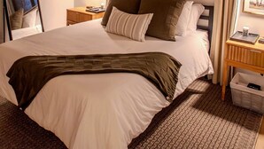 Un dormitorio con cama, ventilador de techo, lámparas de noche, ventana con persianas y mesita de noche con lámpara.