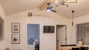 Un espacio habitable moderno con comedor, sofá, sillón, ventilador de techo y puerta que da a un dormitorio.