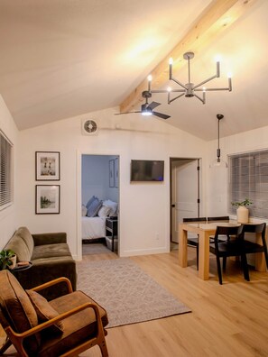 Un espacio habitable moderno con comedor, sofá, sillón, ventilador de techo y puerta que da a un dormitorio.