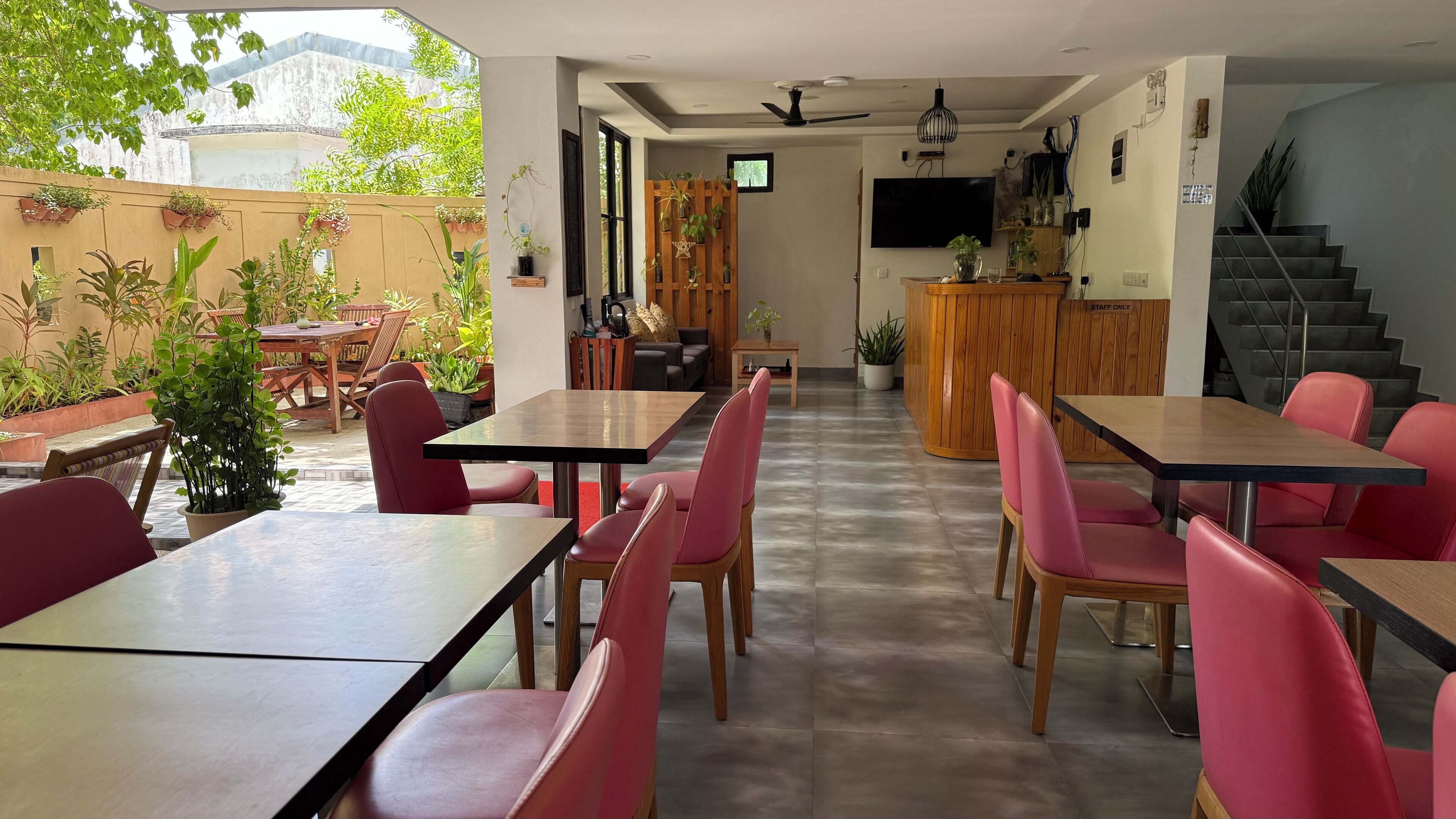 A restaurant with indoor and outdoor seating, wooden tables and chairs, a TV, and a staircase.