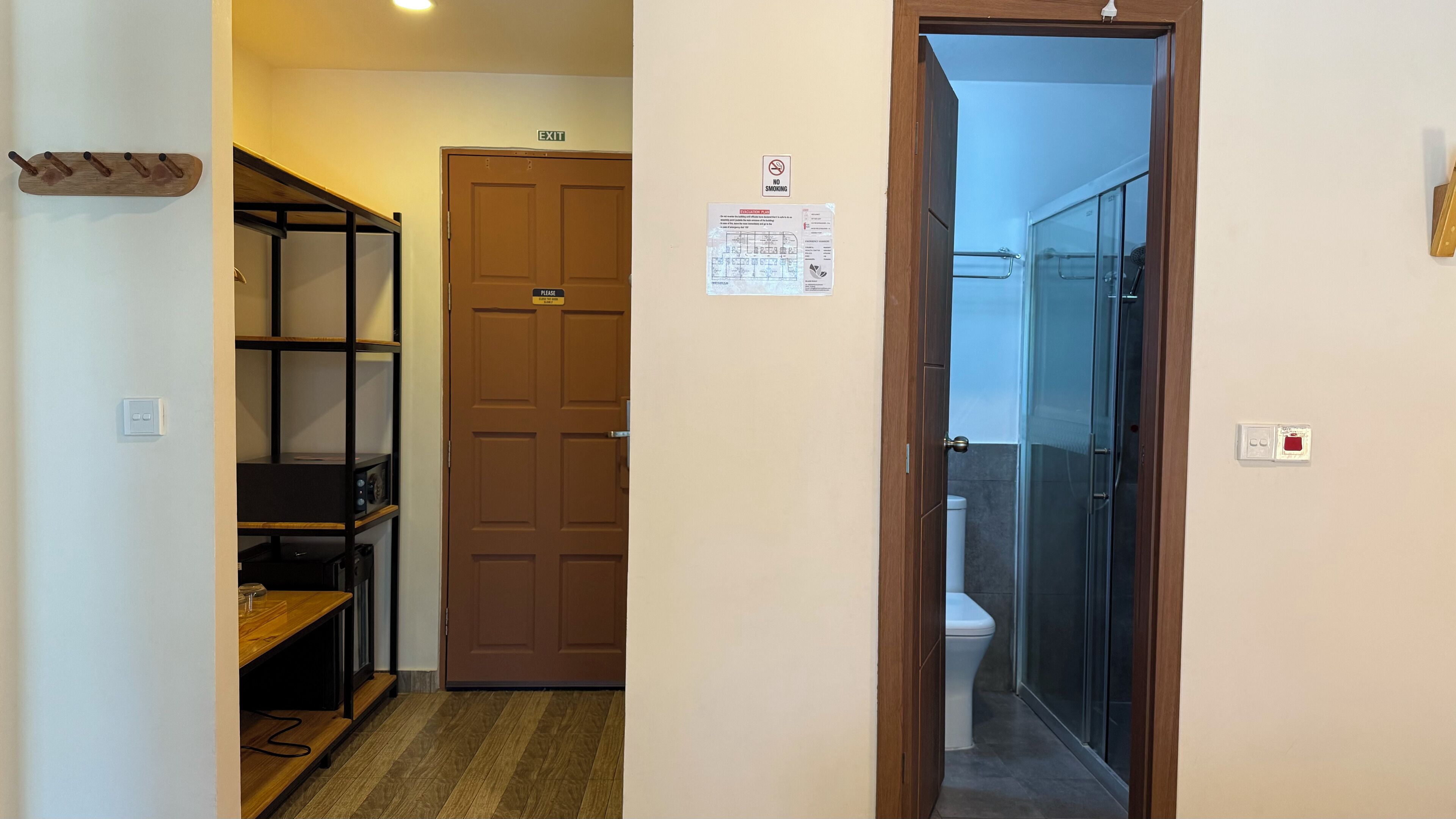 A hallway with a coat rack, a door marked "EXIT," a "NO SMOKING" sign, and a glass-enclosed shower area.