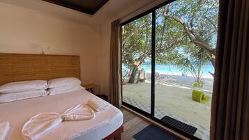 A hotel room with a large bed, a wooden headboard, and a view of a beach with palm trees and a swing chair.