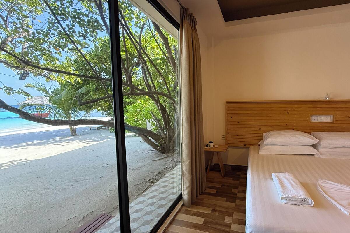 A hotel room with a large window overlooking a beach, a wooden headboard, and neatly made beds.