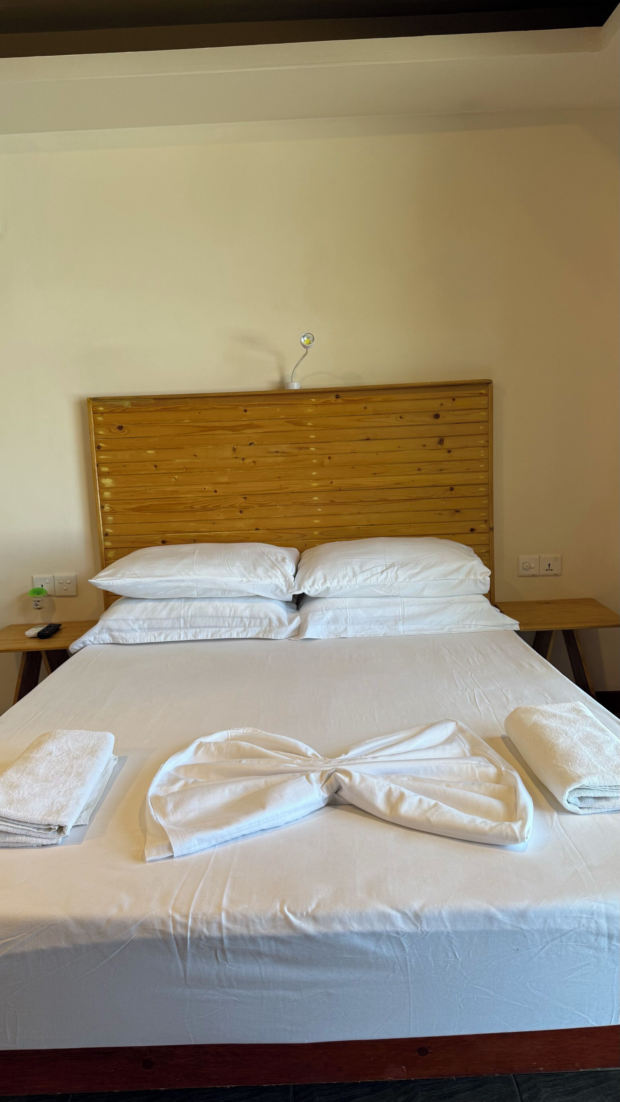 A neatly made bed with white linens and towels, a wooden headboard, and bedside tables with lamps.