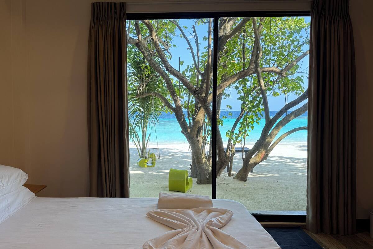 A hotel room with a bed, a view of a beach, and a swing chair.