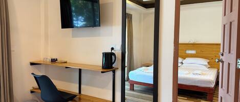 A hotel room with a bed, a desk with a chair, a TV, and a mirror reflecting the room.