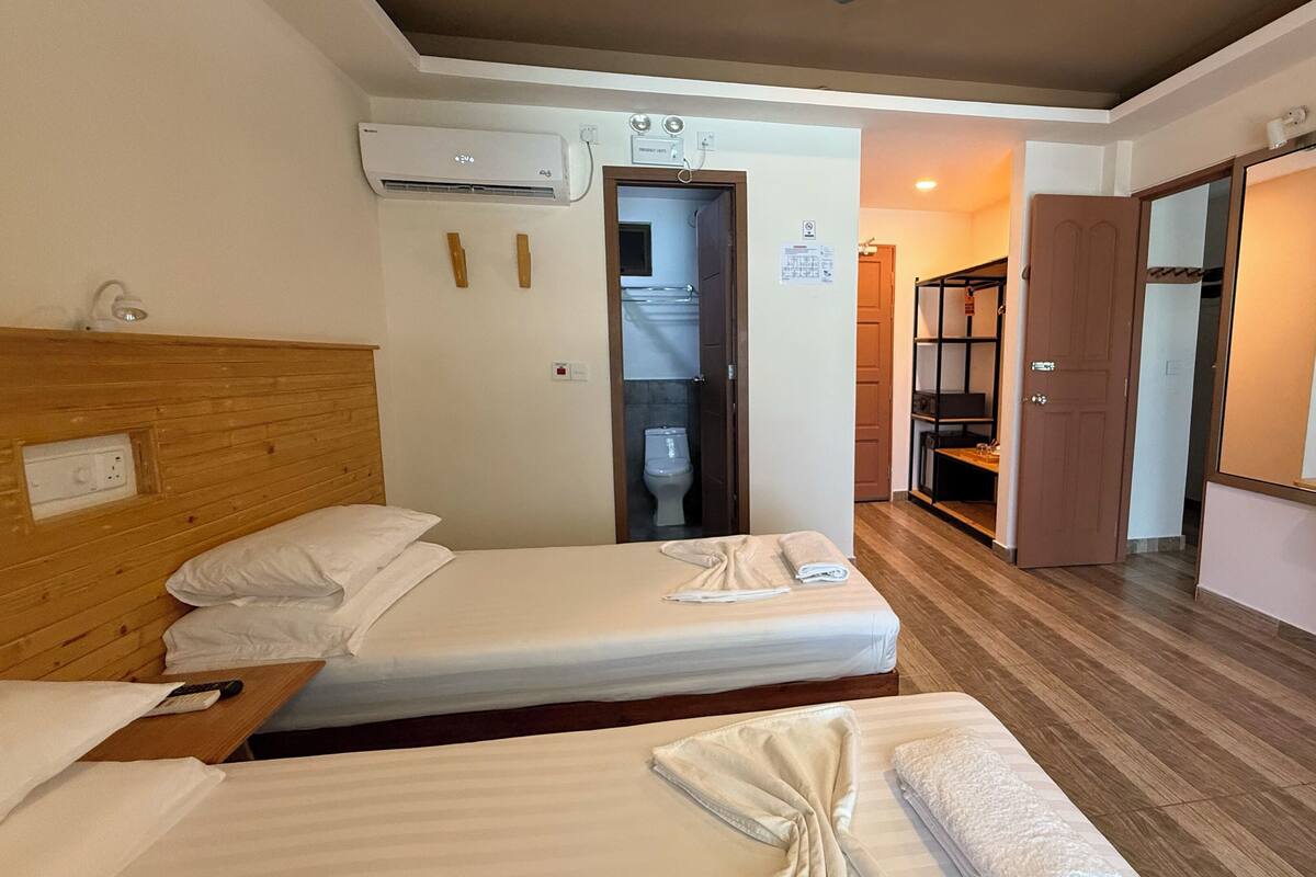 A hotel room with two beds, a wooden headboard, a desk, and a bathroom visible through an open door.
